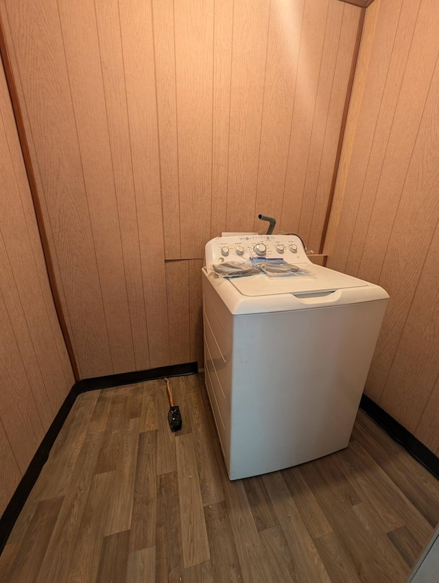 clothes washing area featuring dark hardwood / wood-style flooring, wood walls, and washer / dryer