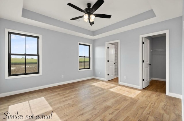 unfurnished bedroom featuring a tray ceiling, a spacious closet, multiple windows, and light hardwood / wood-style flooring