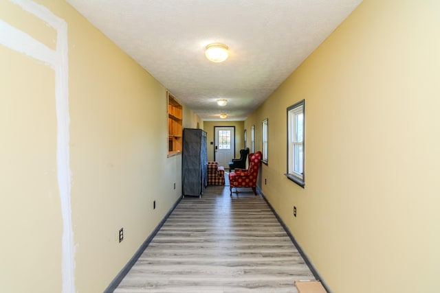 hallway with light wood-type flooring and a textured ceiling