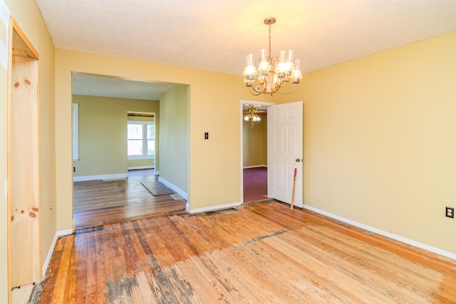 empty room with a notable chandelier, hardwood / wood-style floors, and a textured ceiling