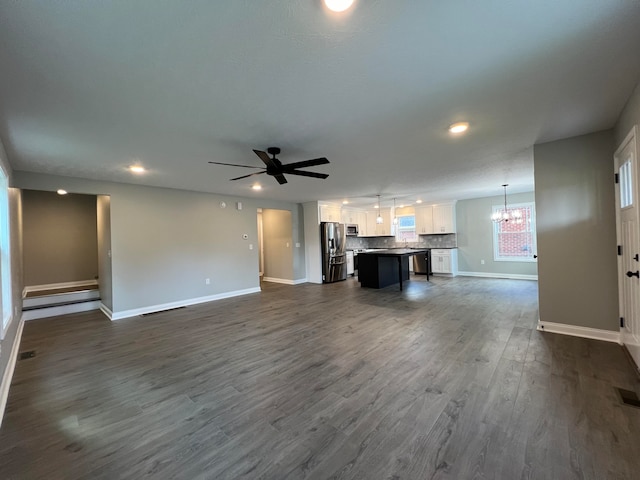 unfurnished living room featuring ceiling fan with notable chandelier and dark hardwood / wood-style flooring