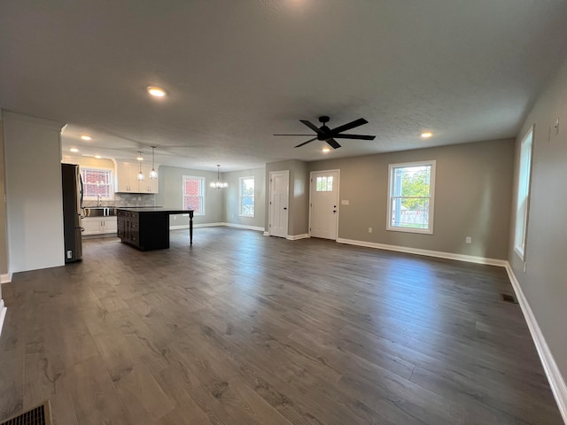 unfurnished living room with a textured ceiling, ceiling fan with notable chandelier, and dark hardwood / wood-style floors