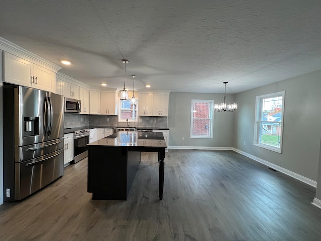 kitchen with pendant lighting, white cabinets, a kitchen island, dark hardwood / wood-style flooring, and stainless steel appliances