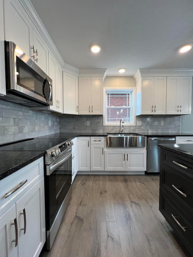 kitchen with white cabinetry, sink, stainless steel appliances, backsplash, and light wood-type flooring