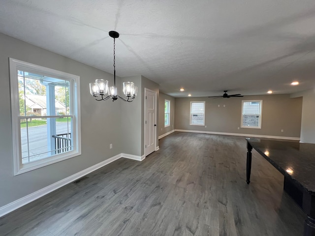 unfurnished dining area featuring a textured ceiling, dark hardwood / wood-style floors, and ceiling fan with notable chandelier