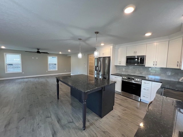 kitchen with appliances with stainless steel finishes, light wood-type flooring, white cabinets, a center island, and hanging light fixtures