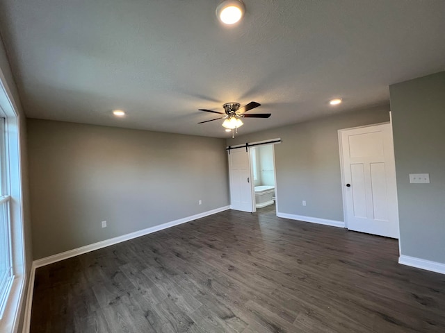 empty room with dark hardwood / wood-style flooring, a barn door, and ceiling fan