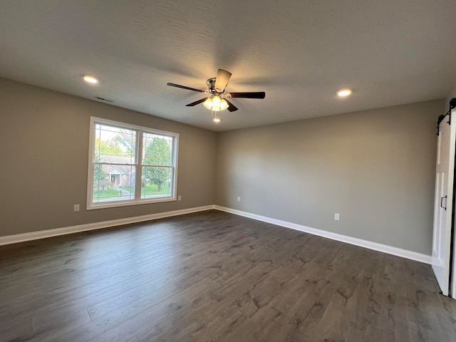 unfurnished room with dark hardwood / wood-style flooring, a barn door, a textured ceiling, and ceiling fan