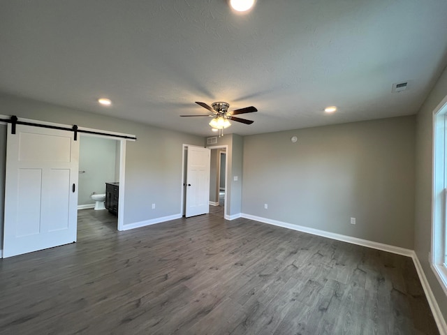 unfurnished bedroom with a barn door, ensuite bath, ceiling fan, and dark wood-type flooring