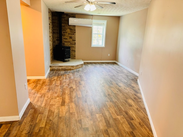 unfurnished living room with ceiling fan, a wood stove, a textured ceiling, light wood-type flooring, and a wall unit AC