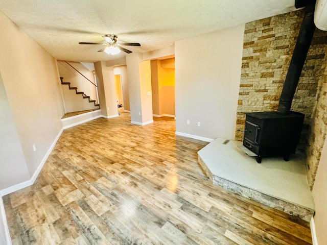 unfurnished living room with wood-type flooring, ceiling fan, a textured ceiling, and a wood stove