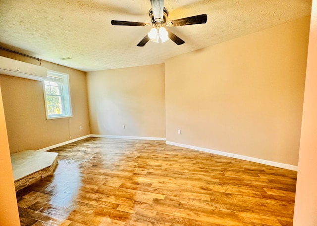 empty room featuring ceiling fan, a wall unit AC, hardwood / wood-style flooring, and a textured ceiling