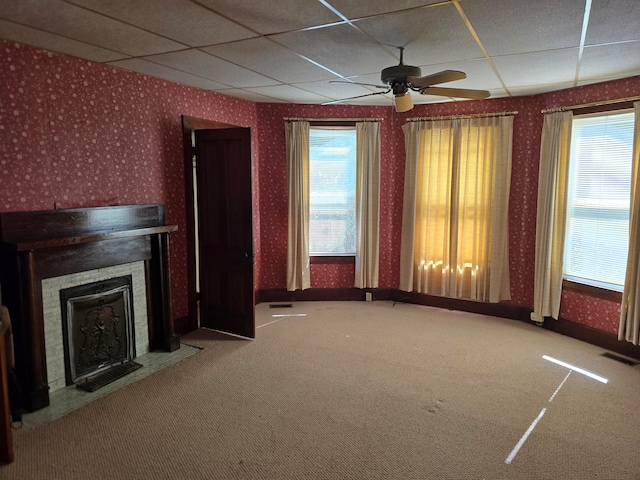 unfurnished living room with ceiling fan, a drop ceiling, and carpet flooring