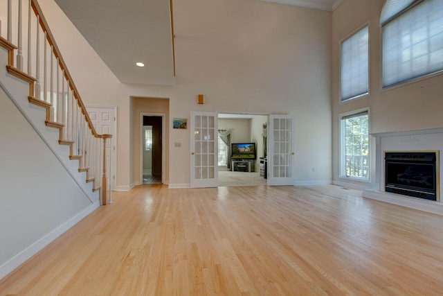 unfurnished living room featuring french doors, a towering ceiling, and light wood-type flooring