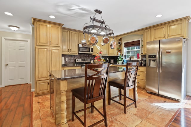 kitchen featuring stainless steel appliances, decorative light fixtures, a breakfast bar area, a kitchen island, and ornamental molding