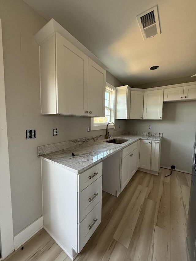 kitchen featuring light stone countertops, white cabinetry, sink, and light hardwood / wood-style flooring