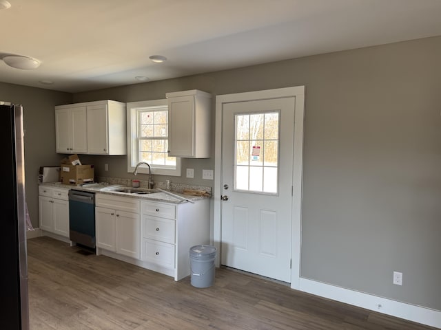 kitchen with stainless steel appliances, light stone counters, a sink, and light wood-style floors