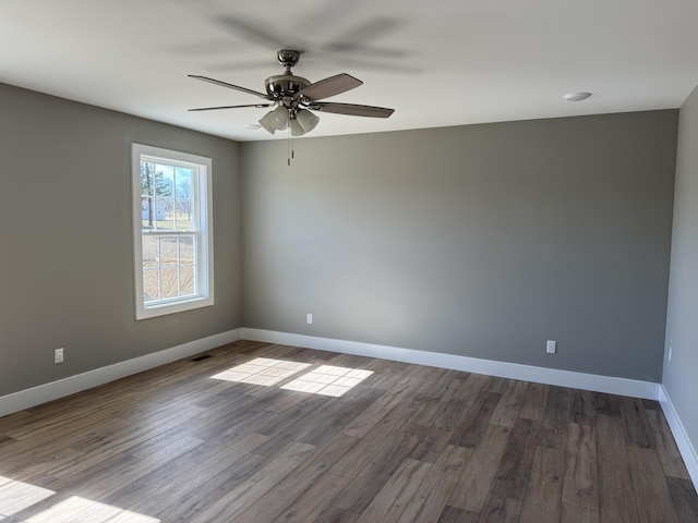 empty room featuring dark wood-style floors, a ceiling fan, and baseboards