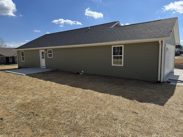 back of property with a shingled roof, a patio area, and a yard