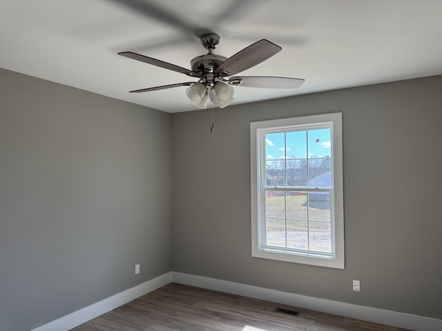 empty room featuring a ceiling fan, visible vents, baseboards, and wood finished floors