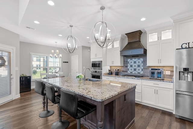 kitchen with an island with sink, white cabinets, stainless steel appliances, and custom range hood