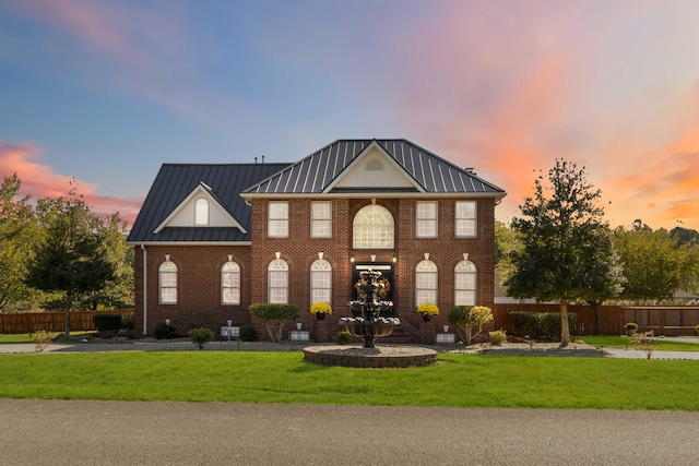view of front of home with brick siding, a standing seam roof, a yard, metal roof, and fence