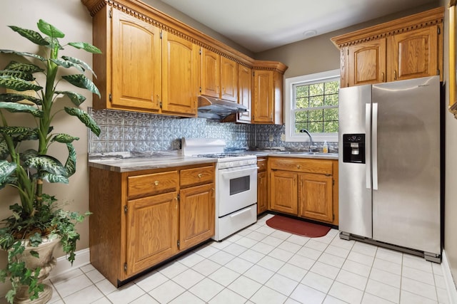 kitchen featuring white range with gas cooktop, under cabinet range hood, a sink, stainless steel fridge, and backsplash