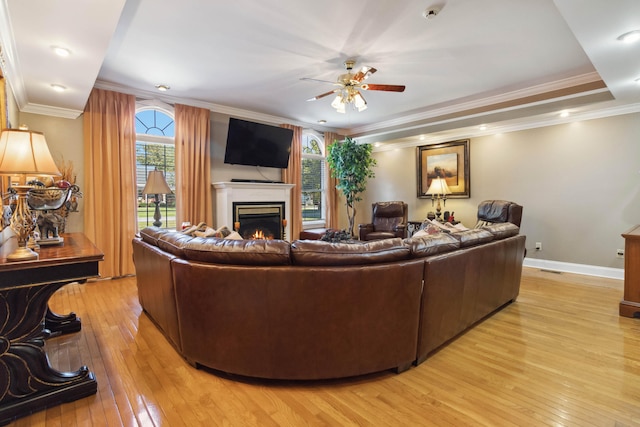 living room with light wood-style floors, ceiling fan, baseboards, and a warm lit fireplace