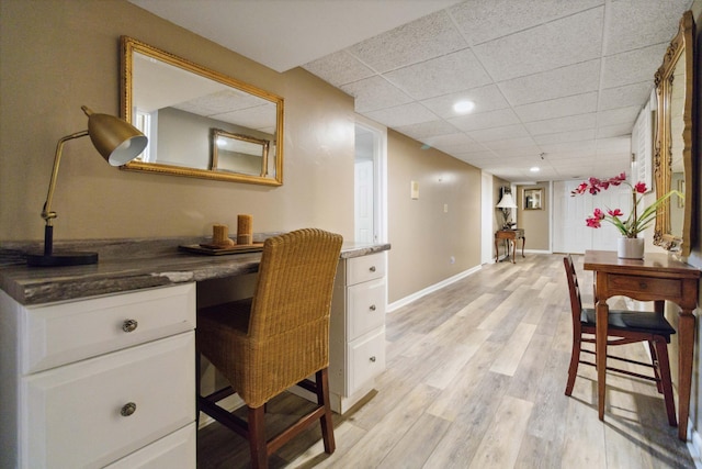 office area with built in study area, a paneled ceiling, light wood-type flooring, and baseboards
