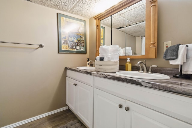 full bath featuring a sink, baseboards, double vanity, and wood finished floors