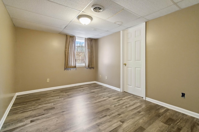 empty room with wood finished floors, baseboards, a drop ceiling, and visible vents