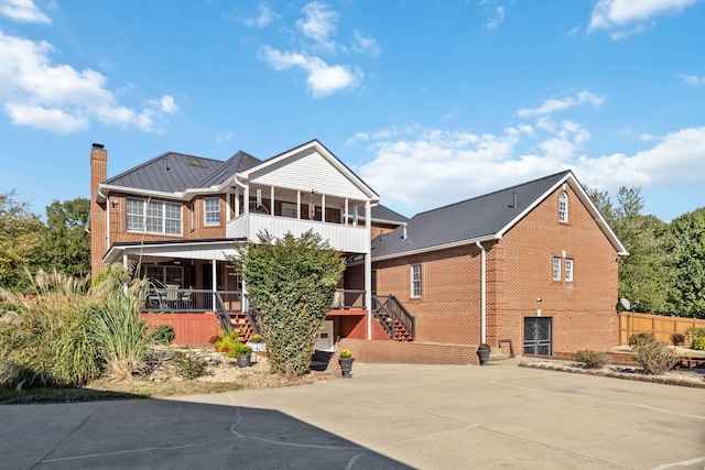 back of house featuring ceiling fan, metal roof, a chimney, stairway, and brick siding