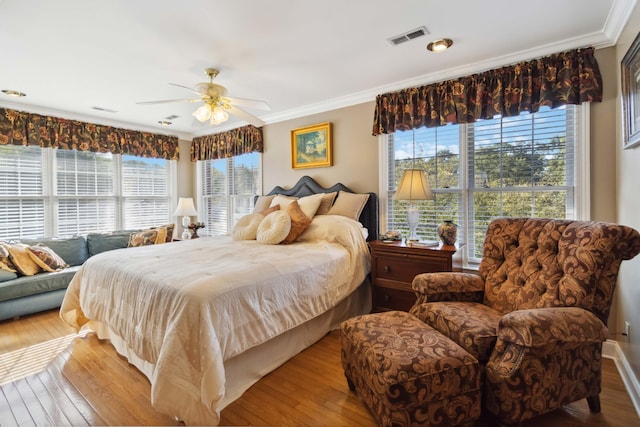 bedroom with multiple windows, wood-type flooring, ornamental molding, and visible vents