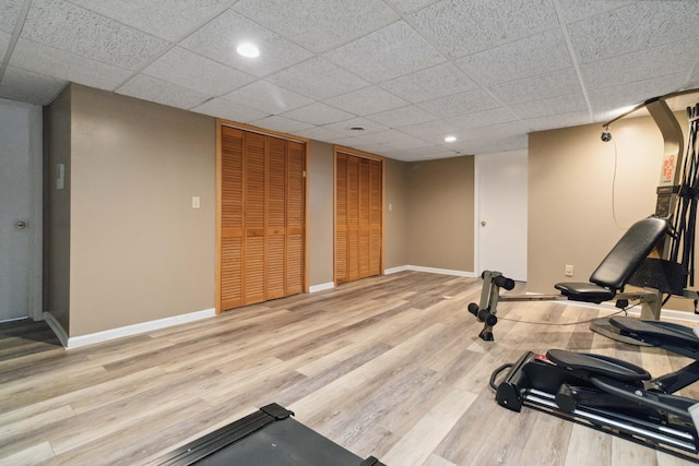 workout area with baseboards, recessed lighting, a paneled ceiling, and light wood-style floors
