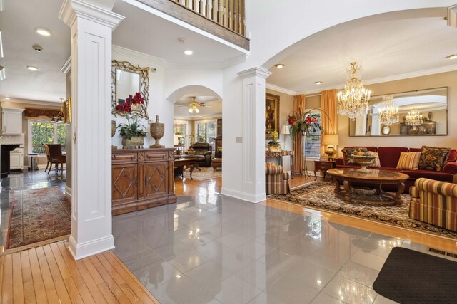 entryway featuring ornate columns, ceiling fan with notable chandelier, crown molding, and arched walkways