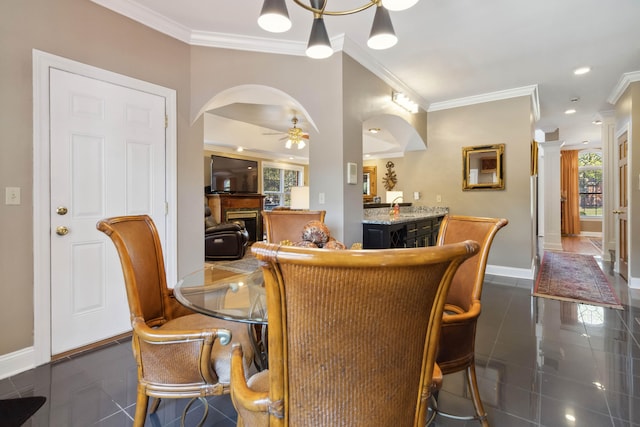 dining room featuring baseboards, arched walkways, a ceiling fan, crown molding, and dark tile patterned flooring