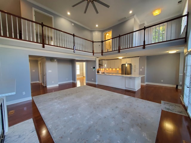 unfurnished living room featuring ceiling fan, sink, ornamental molding, dark wood-type flooring, and a towering ceiling