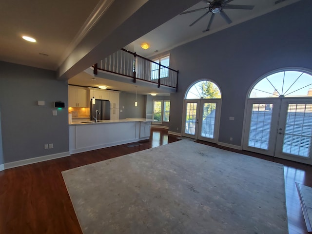 unfurnished living room featuring ceiling fan, french doors, dark hardwood / wood-style floors, sink, and a high ceiling