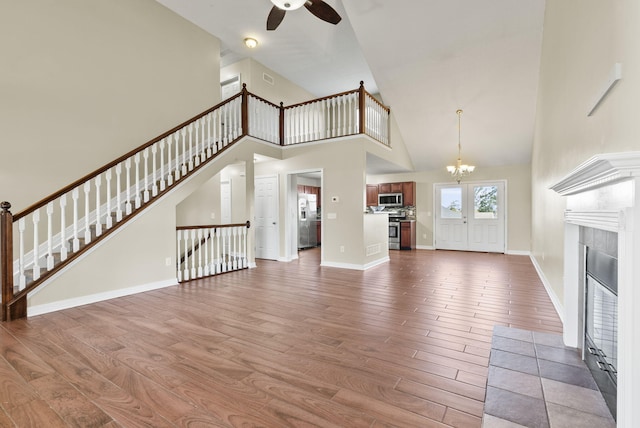 unfurnished living room with ceiling fan with notable chandelier, high vaulted ceiling, a fireplace, and hardwood / wood-style floors