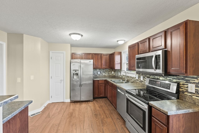 kitchen featuring light hardwood / wood-style floors, a textured ceiling, stainless steel appliances, and sink