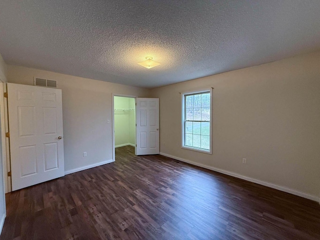 unfurnished bedroom featuring visible vents, a textured ceiling, dark wood finished floors, baseboards, and a spacious closet