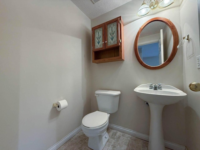 bathroom featuring visible vents, toilet, a sink, a textured ceiling, and baseboards