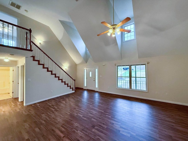 unfurnished living room with visible vents, baseboards, stairway, a towering ceiling, and wood finished floors