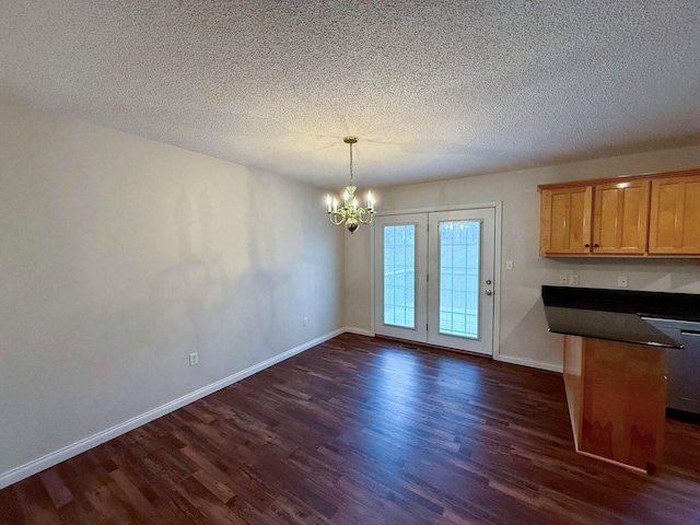 unfurnished dining area featuring a textured ceiling, dark wood-style floors, baseboards, and a chandelier