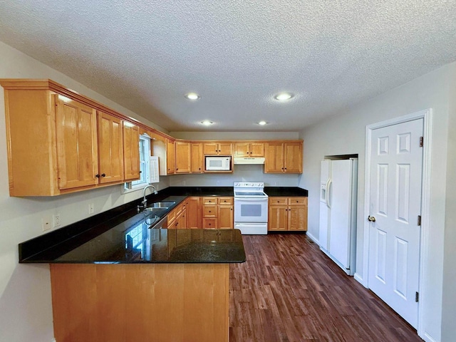 kitchen with white appliances, a peninsula, a sink, dark wood-type flooring, and under cabinet range hood