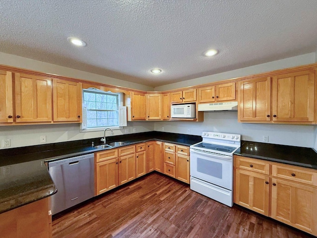 kitchen with under cabinet range hood, recessed lighting, dark wood-style floors, white appliances, and a sink