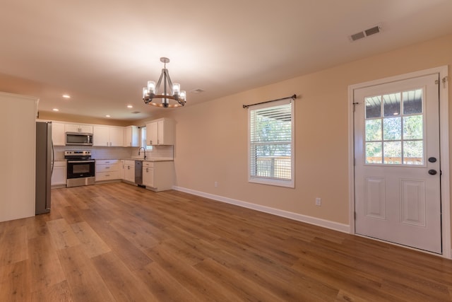 kitchen with stainless steel appliances, decorative light fixtures, a wealth of natural light, and white cabinetry