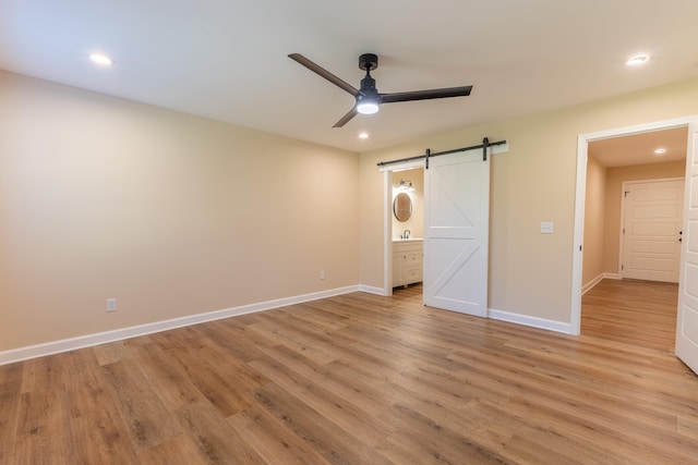 unfurnished bedroom featuring ceiling fan, light hardwood / wood-style floors, a barn door, and ensuite bathroom