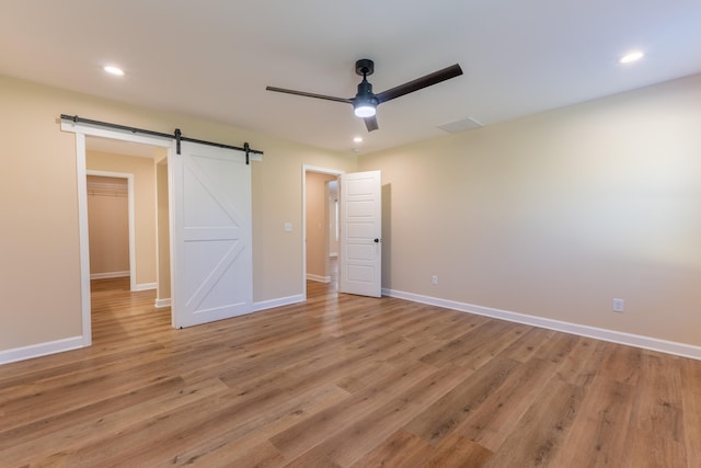 unfurnished bedroom with ceiling fan, a closet, a spacious closet, light wood-type flooring, and a barn door