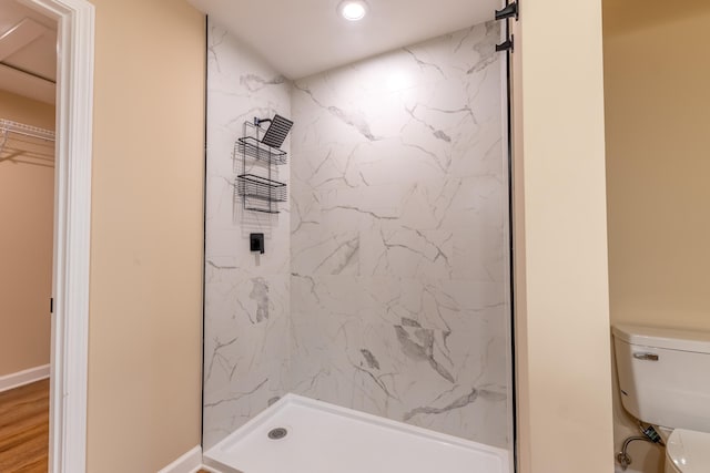 bathroom featuring tiled shower, toilet, and wood-type flooring